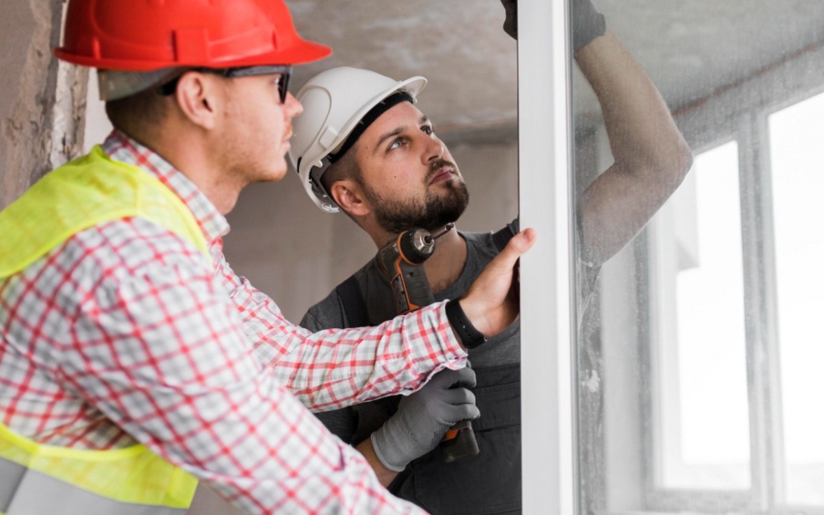 Profissionais instalando uma esquadria envidraçada em uma obra